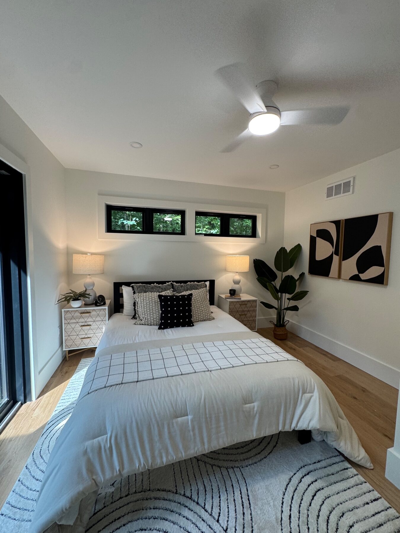 Bright guest bedroom staged in white with black accents and greenery