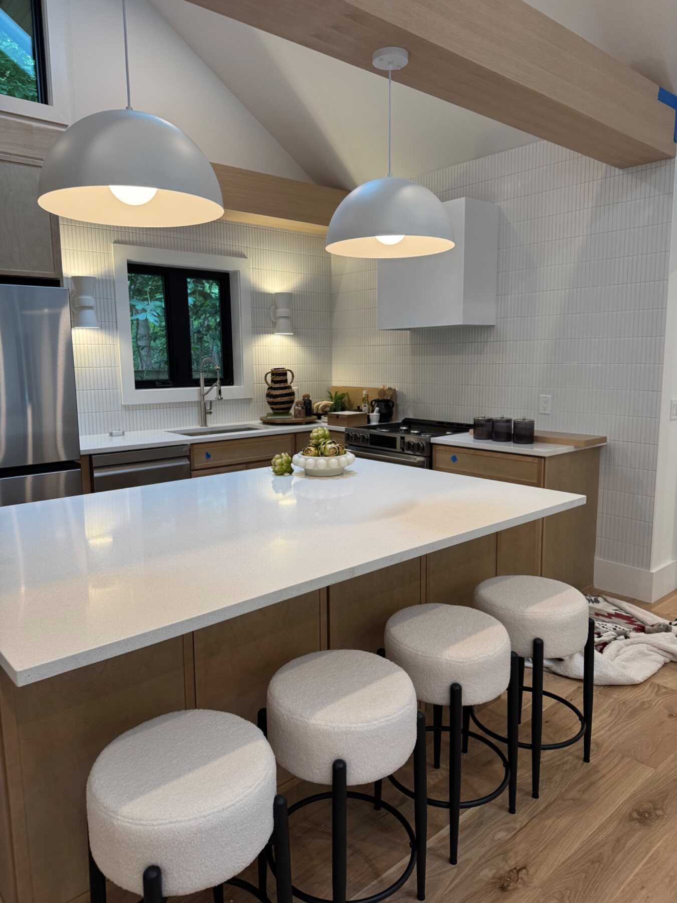 Modern kitchen styled with warm wood cabinetry, white counters and sculptural pendants